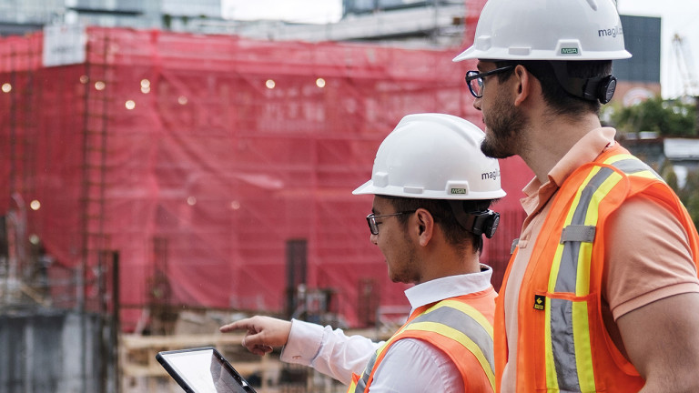 Two construction workers pointing at the construction site while using a tablet