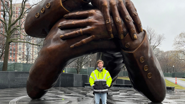A man in a reflective jacket standing under a statue of hands